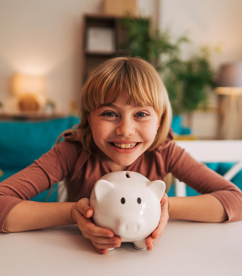 Young girl joyfully holding savings piggy bank.