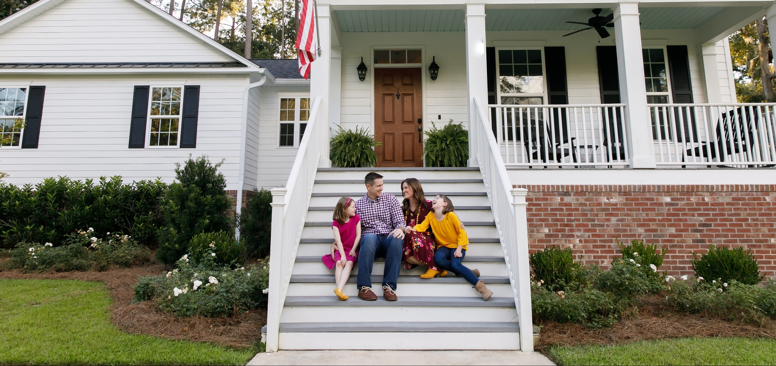 Family standing outside front of new construction white siding farmhouse in the suburbs