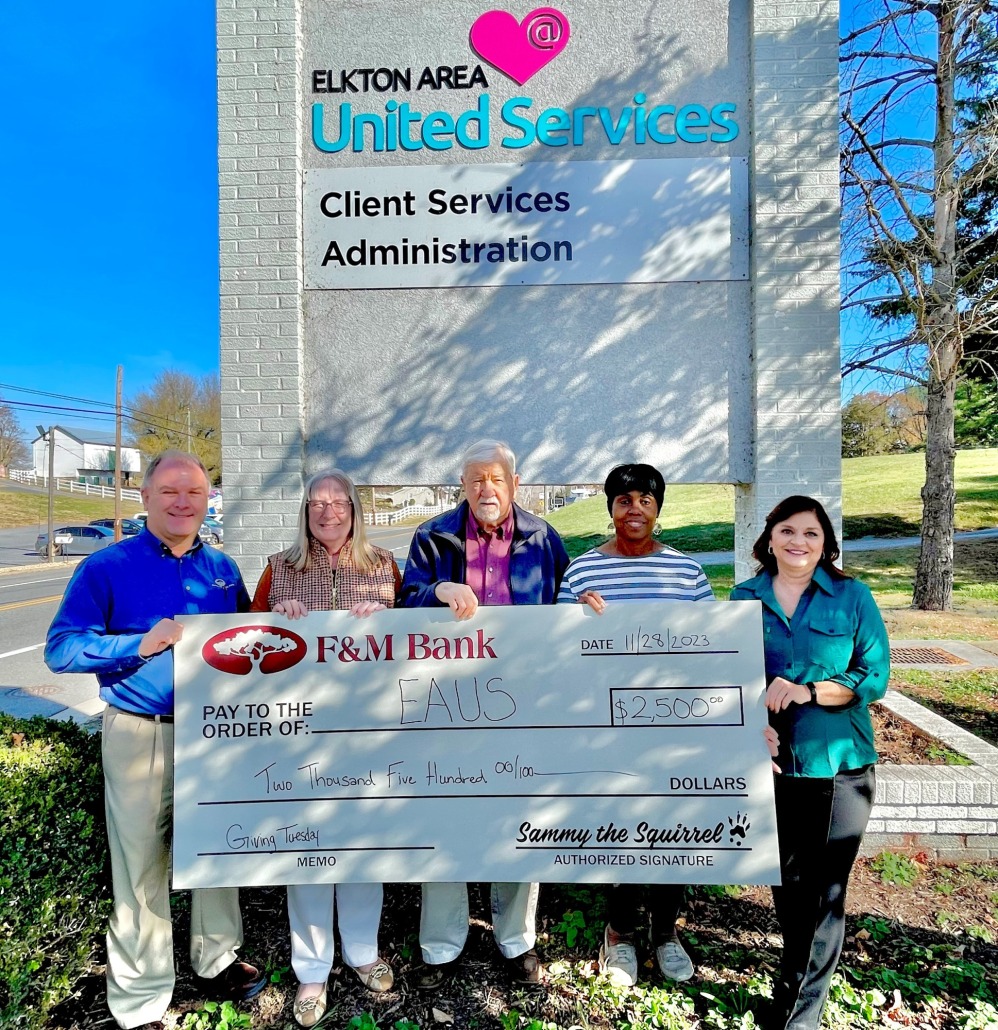 Board members and F&M bank employees hold a donation check in front of EAUS building sign